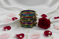 Stack of colorful bangles with a red rose and petals on a white fabric background